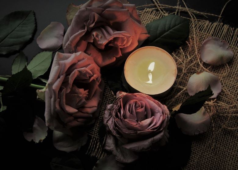 Pink roses and a small lit candle arranged on burlap cloth, cremation services Garyville, LA